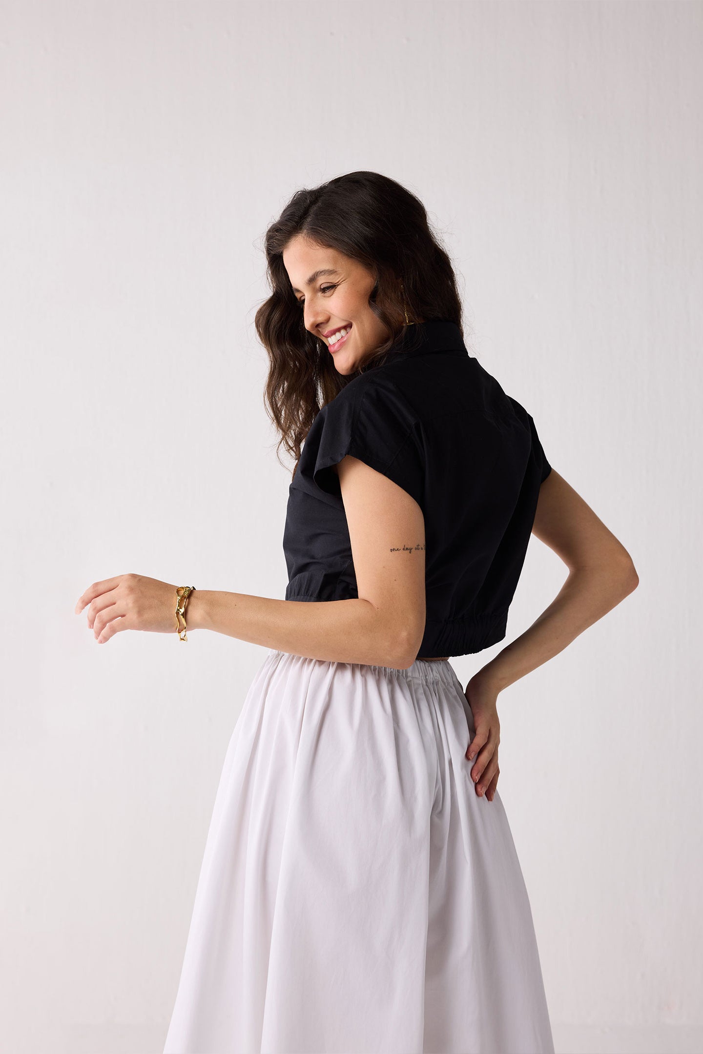 Woman wearing a black top and white skirt against a plain background