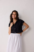 Woman wearing a black top and white skirt against a plain background