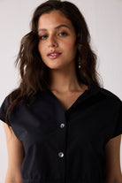 Woman wearing a black short-sleeve blouse with buttons on a white background