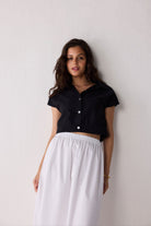 Woman wearing a black top and white skirt against a plain background