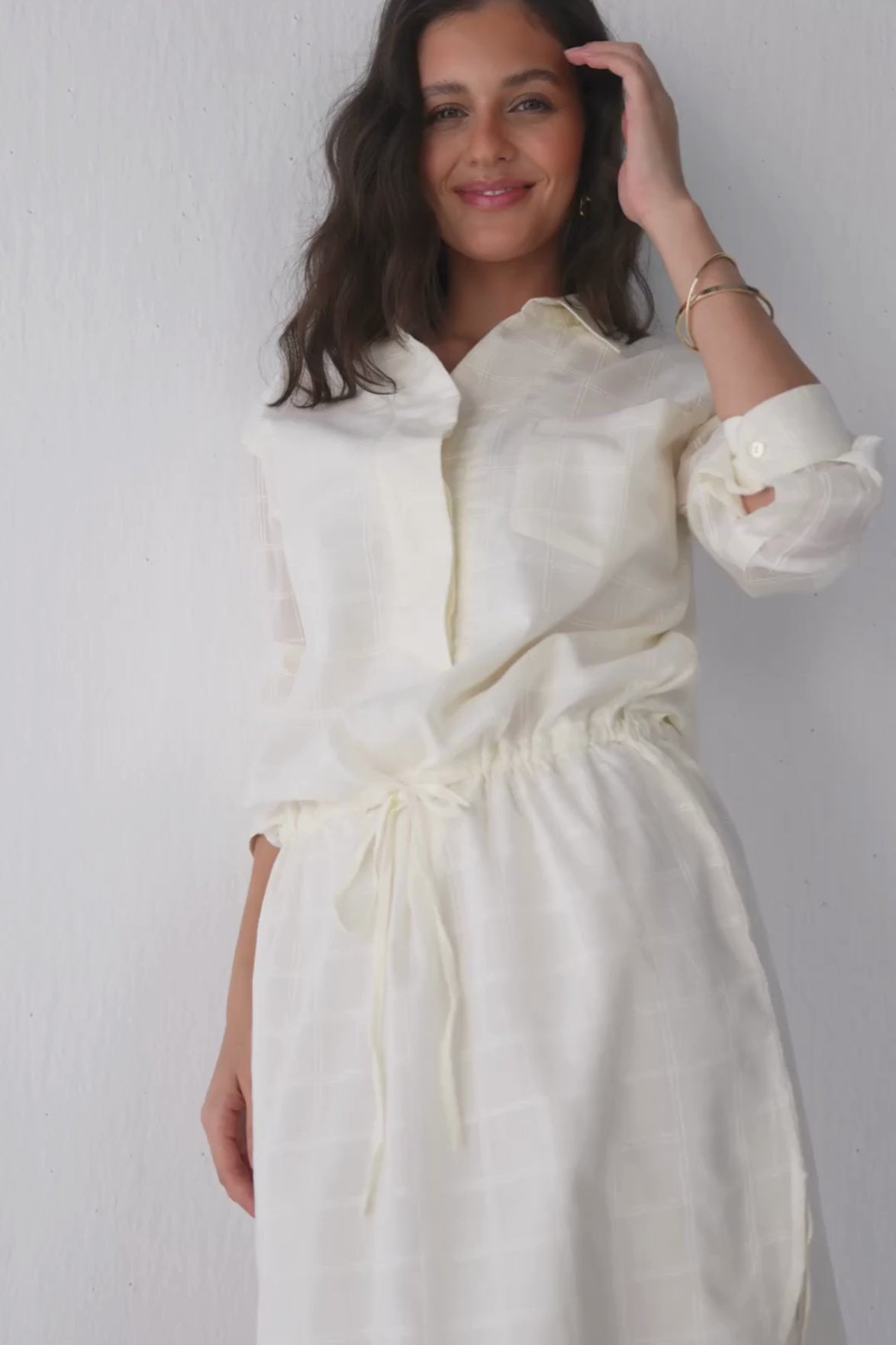 Fashion model wearing Reistor Meet Me by the Cliff dress in off-white, standing and moving naturally to showcase the dress’s relaxed silhouette, soft flowing fabric, and subtle movement, highlighting its effortless drape and resort-ready style.