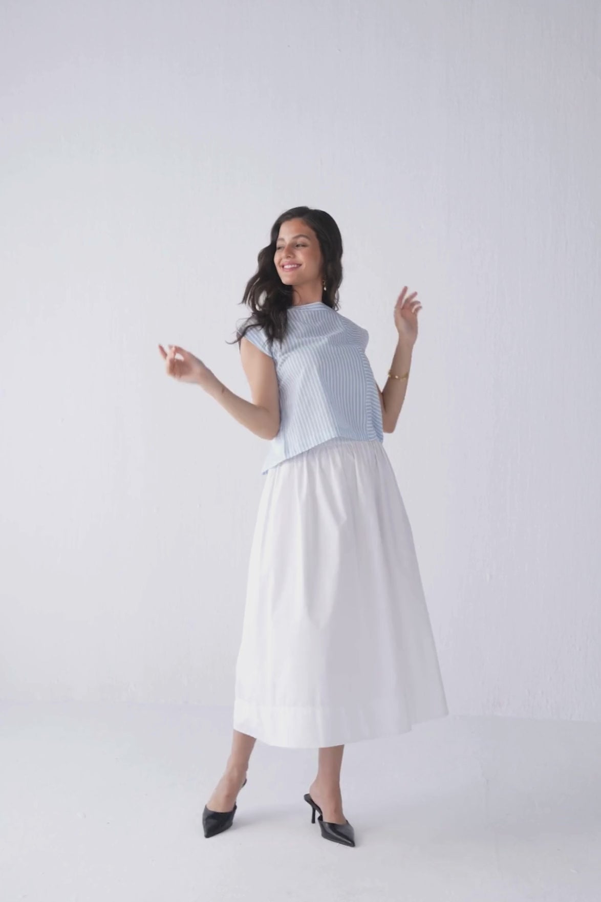 Model showcases Reistor Button-Back Crew Neck Top in blue stripes, posing to highlight the soft fabric, classic crew neckline, vertical stripe pattern, and functional button-back design.