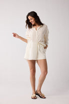 A woman wearing an off-white shirt and shorts on a plain background