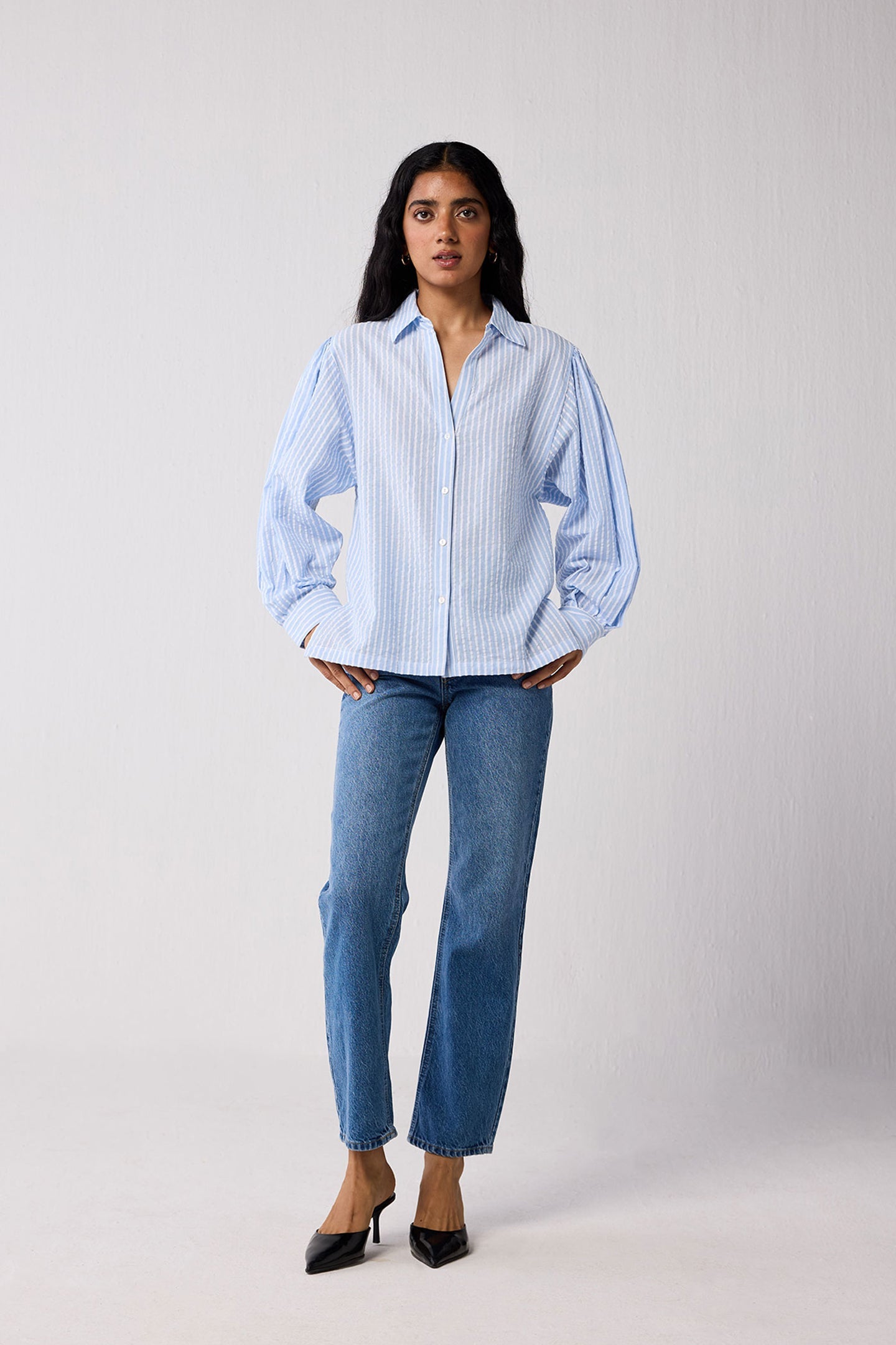 Woman wearing a light blue striped shirt and jeans on a white background