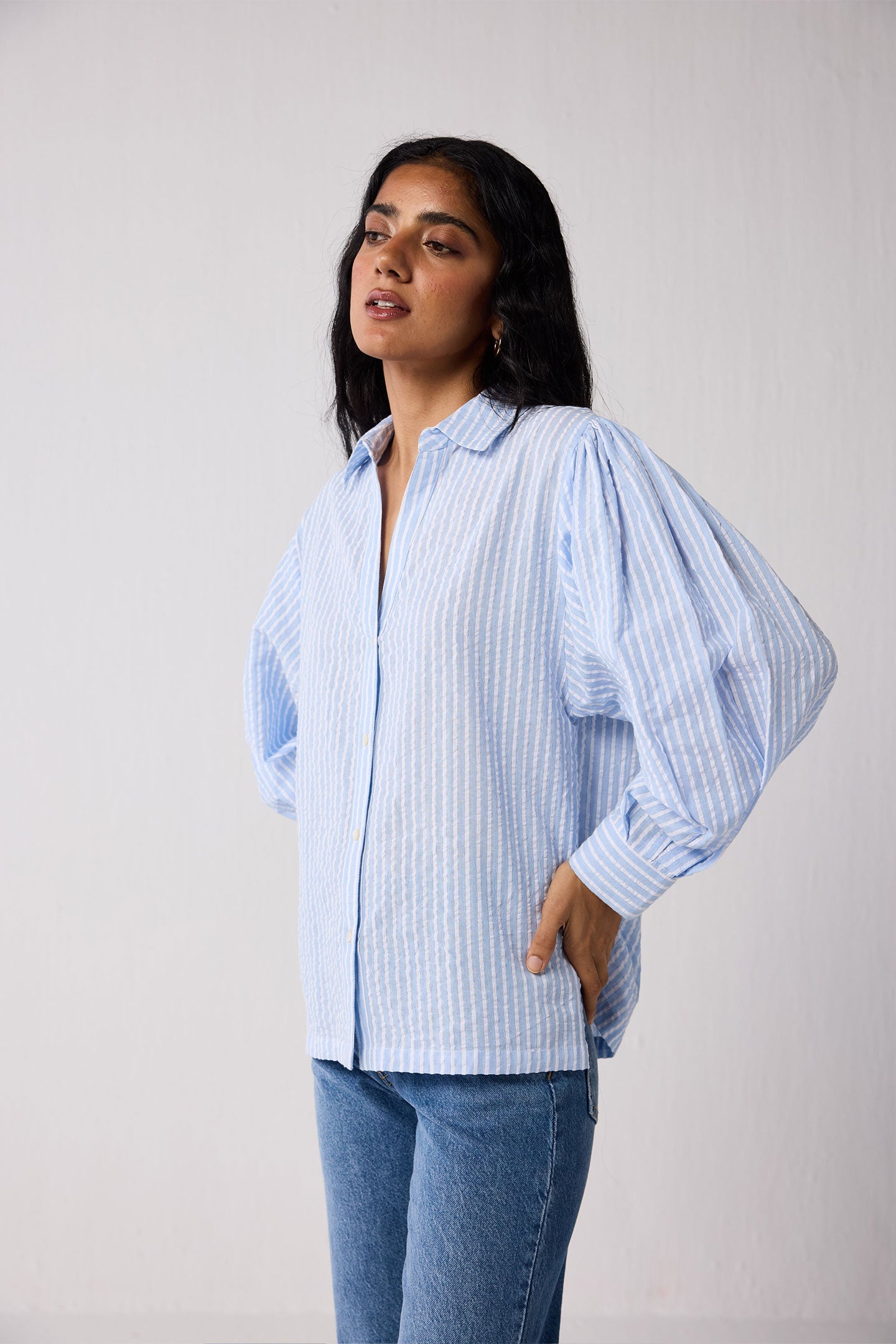 Woman wearing a light blue striped shirt and jeans on a white background