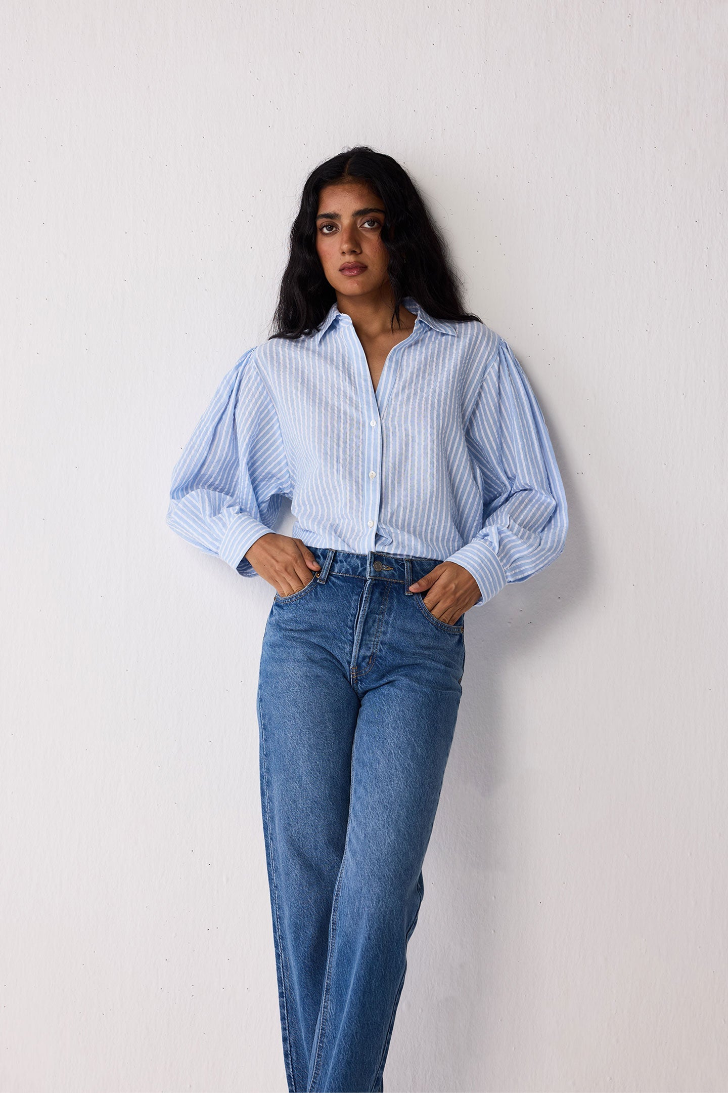 Woman wearing a light blue striped shirt and jeans on a white background