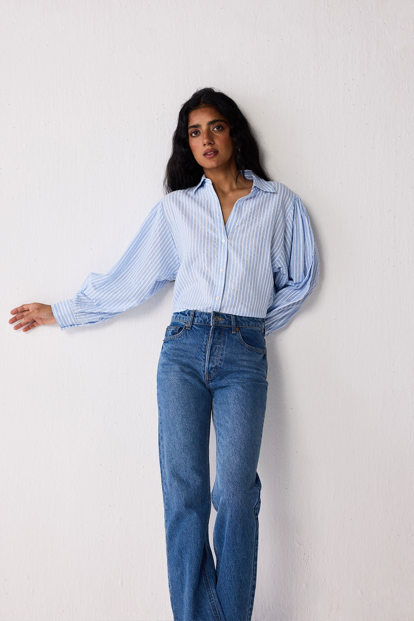 Woman wearing a light blue striped shirt and jeans on a white background