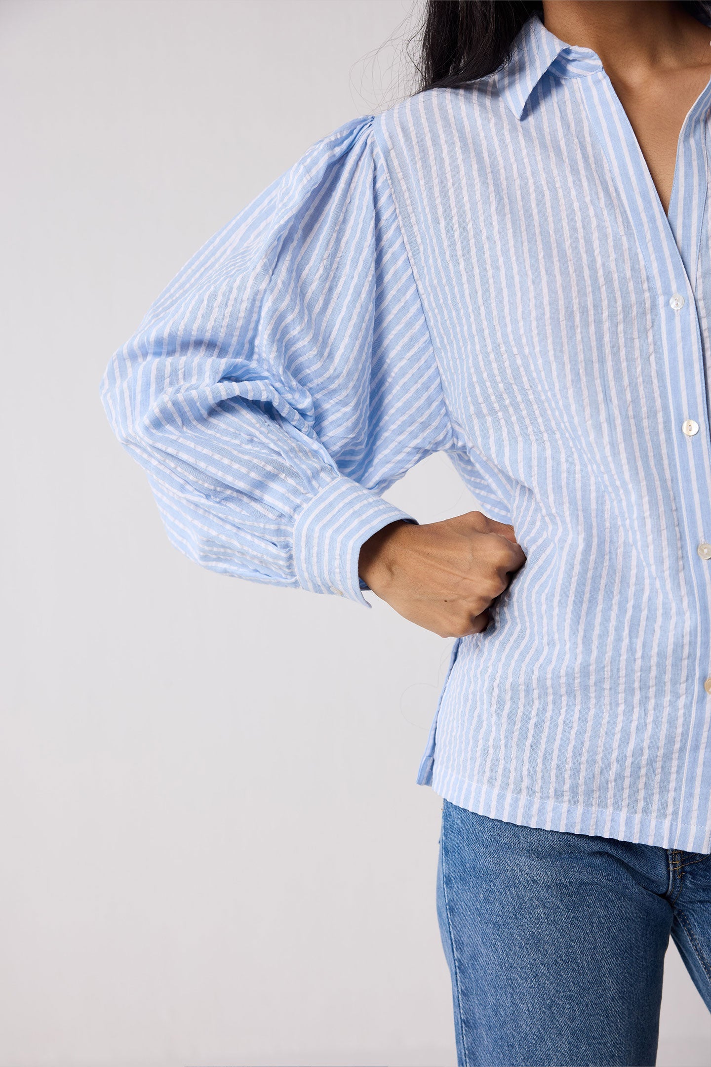 Woman wearing a light blue striped shirt and jeans on a white background