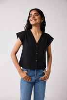 Woman wearing a black top and blue jeans against a plain background
