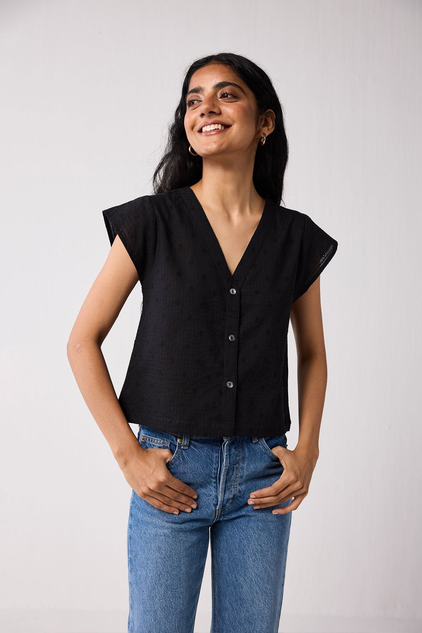 Woman wearing a black top and blue jeans against a plain background